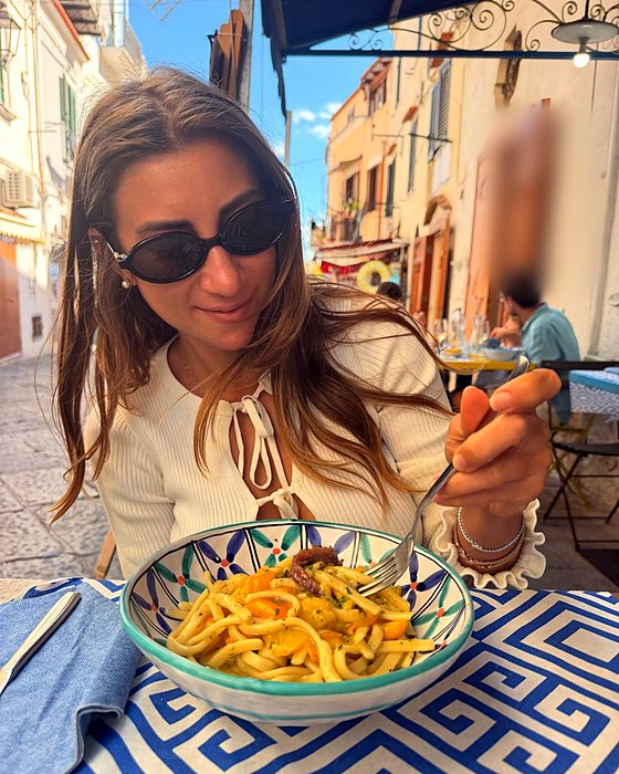 Una ragazza con una forchetta davanti a una ciotola di pasta, a un tavolo all'aperto