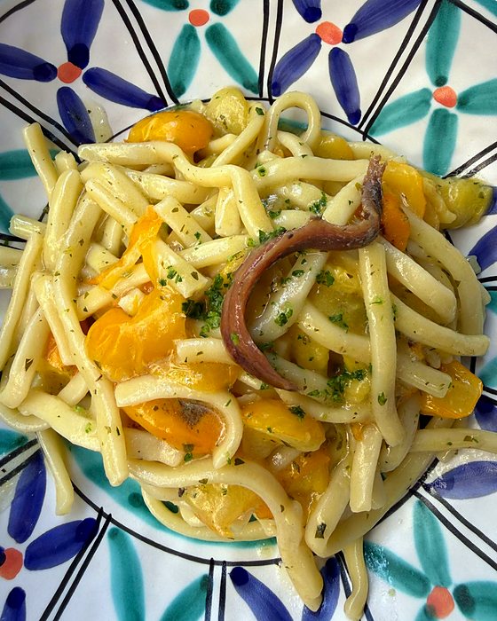 Un piatto decorato di scialatelli con colatura di alici e pomodorini gialli