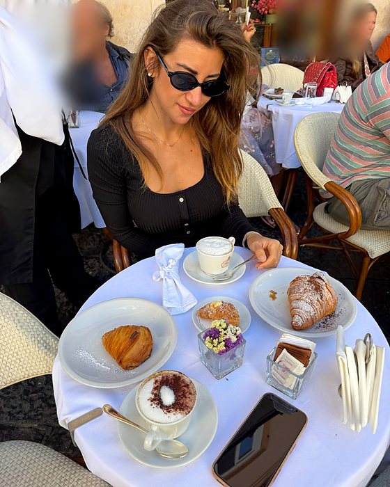 Una ragazza a un tavolino con cappuccino e cornetti