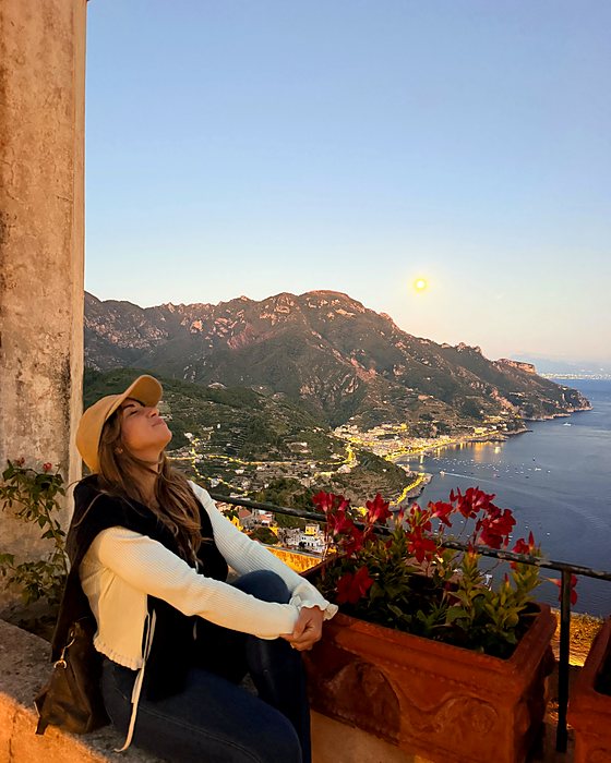 Una ragazza seduta tra i fiori a Villa Rufolo, con la costa e la luna sullo sfondo