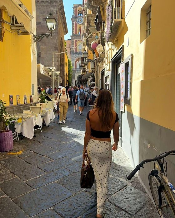 Una ragazza di spalle in un vicolo di Sorrento con i tavolini e le case gialle