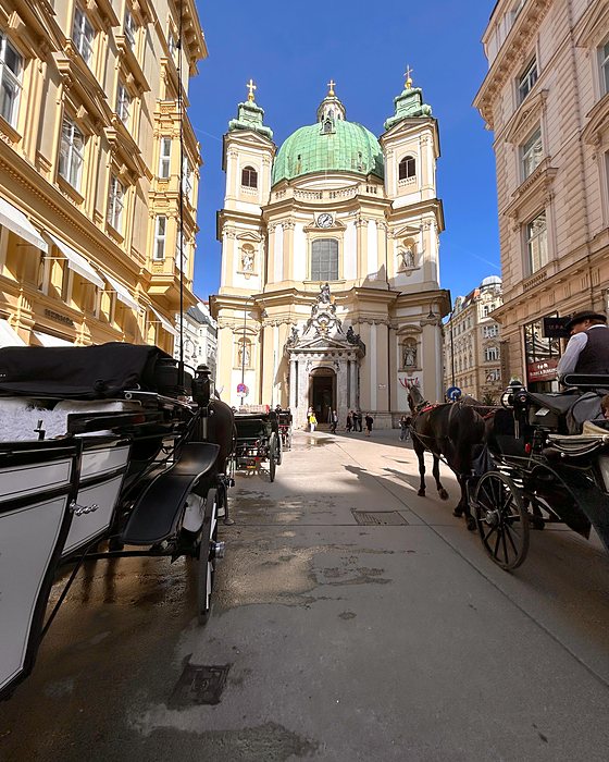 The Peterskirche with its green dome and horse carriages in the foreground